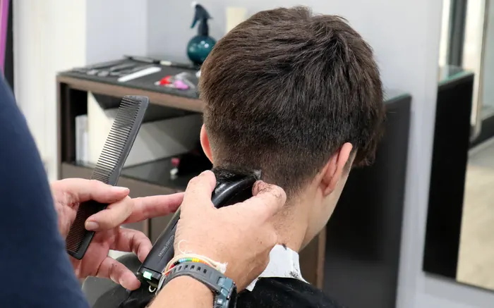 El barbero sujeta el peine y pasa la máquina por la nuca de un cliente joven.